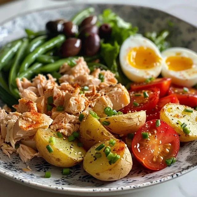 Side view of a fresh Nicoise Salad with tuna, hard-boiled eggs, and sliced tomatoes.