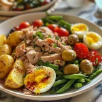 Side view of a colorful Tuna Niçoise salad garnished with fresh herbs and olives.