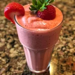 A detailed view of a strawberry smoothie, highlighting chunks of strawberries and a creamy froth.