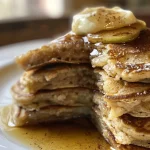 A stack of golden-brown apple and cinnamon pancakes topped with diced apples and syrup.