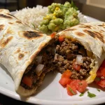 Close-up of a juicy beef burrito filled with meat, rice, and beans.