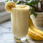 Close-up of a creamy banana smoothie in a glass, with a banana slice on top.