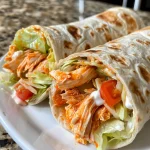 A close-up side view of a buffalo chicken wrap filled with shredded chicken, lettuce, and tomatoes.