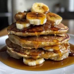 A close-up side view of caramel banana pancakes topped with caramel sauce and banana slices.