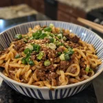 A close-up view of a bowl of Chili Garlic Beef Noodles with finely sliced green onions on top.