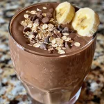 Close-up of a chocolate banana oat smoothie in a glass, featuring a creamy texture and garnished with banana slices.
