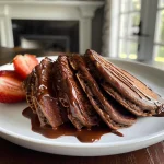 Close-up of stacked chocolate protein pancakes drizzled with maple syrup.