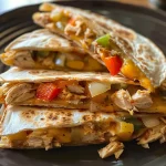 Close-up view of golden-brown chicken quesadillas with melted cheese and colorful diced peppers.