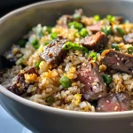 Close-up of Garlic Butter Steak Fried Rice in a bowl, featuring juicy pieces of steak and green onions.