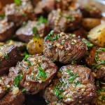 Close-up view of juicy Garlic Parmesan Steak Bites garnished with parsley, next to creamy mashed potatoes.