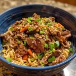 Close-up of sticky beef noodles garnished with green onions and sesame seeds.