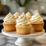 Close-up side view of moist vanilla cupcakes topped with creamy frosting.