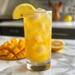 Side view of a refreshing glass of Mango Lemonade with ice and a slice of lemon.