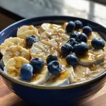 ['Side view of a Blueberry Banana Protein Pancake Bowl topped with fresh blueberries and peanut butter.', 'Close-up of a colorful pancake bowl featuring bananas, blueberries, and creamy peanut butter.', 'Delicious Blueberry Banana Protein Pancake Bowl with a rich texture and vibrant fruit toppings.', 'A hearty stack of protein pancakes adorned with blueberries and a drizzle of maple syrup.']