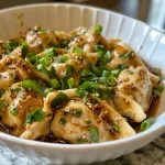 ['Close-up view of golden-brown Cilantro Ginger Chicken Wontons on a plate.', 'Side view of juicy Cilantro Ginger Chicken Wontons garnished with cilantro.', 'Crispy wontons filled with ground chicken, cilantro, and ginger.', 'Appetizing Cilantro Ginger Chicken Wontons served with chili sauce.']