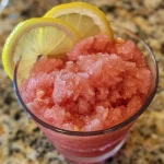 ['Close-up view of a refreshing frozen watermelon lemonade in a glass with lemon slices.', 'A vibrant glass of frozen watermelon lemonade with ice, garnished with lemon wedges.', 'Side view of a colorful watermelon lemonade, showcasing frosty texture and fresh ingredients.', 'Iced watermelon lemonade with a smooth consistency, presented in a clear glass with lemon garnish.']