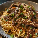 ['Close-up of juicy sticky beef noodles with a glossy glaze and colorful toppings.', 'Side view of a bowl filled with sticky beef noodles, showcasing tender beef and green onions.', 'Detailed image of sticky beef noodles, highlighting the rich sauce and garnishes.', 'Close-up of a delicious plate of sticky beef noodles, displaying vibrant colors and textures.']
