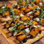 ['Close-up view of a butternut squash flatbread topped with kale, garlic, and pancetta.', 'Side view of a golden-brown flatbread featuring butternut squash and melted mozzarella.', 'Delicious flatbread showcasing roasted butternut squash, crispy pancetta, and fresh greens.', 'Appetizing flatbread slice highlighting vibrant ingredients like kale and roasted garlic.']