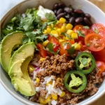 ['A colorful Ground Beef Burrito Bowl featuring various fresh ingredients in a ceramic bowl.', 'Overhead view of a Ground Beef Burrito Bowl filled with rice, beans, vegetables, and garnishes.', 'Close-up of a juicy Ground Beef Burrito Bowl with vibrant toppings and a sprinkle of cilantro.', 'Side view of a Ground Beef Burrito Bowl showcasing layers of beef, cheese, and fresh avocado.']
