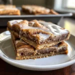['Side view of healthy cinnamon roll cookie bars, displaying a soft, moist texture with cinnamon swirls.', 'Close-up of healthy cinnamon roll cookie bars, highlighting the golden brown edges and creamy topping.', 'Image of healthy cinnamon roll cookie bars, showcasing their fluffy interior and drizzle of cream cheese frosting.', 'Detailed view of healthy cinnamon roll cookie bars, illustrating the cinnamon dusting and rich coloration.']