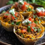 ['Close-up view of small taco cups filled with ground beef, cheese, and toppings.', 'Delicious Lil Taco Cups showing a side view with colorful toppings and melted cheese.', 'Juicy taco cups made from tortillas, filled with beef, cilantro, and diced tomatoes.', 'Side view of golden-brown taco cups garnished with sour cream and fresh ingredients.']