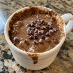 ['Close-up of a delicious protein mug cake with chocolate chips on top.', 'Side view of a moist protein mug cake in a white mug, showcasing its rich texture.', 'Juicy protein mug cake in a mug, highlighting its fluffy and chocolatey interior.', 'Image of a protein mug cake with a glossy finish and chocolate chips, served fresh.']