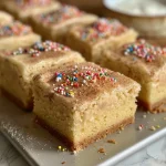 ['A close-up view of Vanilla Chai Sugar Cookie Bars with a soft, chewy texture, sprinkled with colorful holiday decorations.', 'Side view of decadent Vanilla Chai Sugar Cookie Bars, showcasing their golden-brown edges and creamy frosting.', 'Juicy and inviting Vanilla Chai Sugar Cookie Bars, topped with festive sprinkles, presented on a white plate.', 'A tempting slice of Vanilla Chai Sugar Cookie Bars displaying layers of spices and sweetness, garnished with bright holiday sprinkles.']