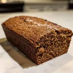 ['Close-up view of a moist vegan gingerbread loaf on a plate.', 'Slice of vegan gingerbread loaf with icing and spices on a wooden table.', 'Side view of a sliced vegan gingerbread loaf with a creamy topping.', 'Juicy and fluffy vegan gingerbread loaf with a dusting of powdered sugar.']