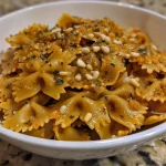 ['A close-up view of creamy vegan pumpkin pasta topped with pine nuts and fresh sage.', 'Side angle of a bowl featuring vegan pumpkin pasta with a vibrant orange sauce and pasta shapes.', 'Detailed shot of vegan pumpkin pasta garnished with pine nuts and herbs, with a rustic bowl.', 'Close-up of a delicious serving of vegan pumpkin pasta, showcasing its rich texture and ingredients.']