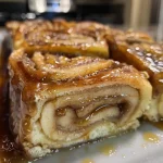 A close-up side view of a caramel apple roll, showcasing its golden-brown exterior and gooey caramel topping.