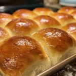 Close-up view of golden brown honey wheat dinner rolls on a rustic surface.
